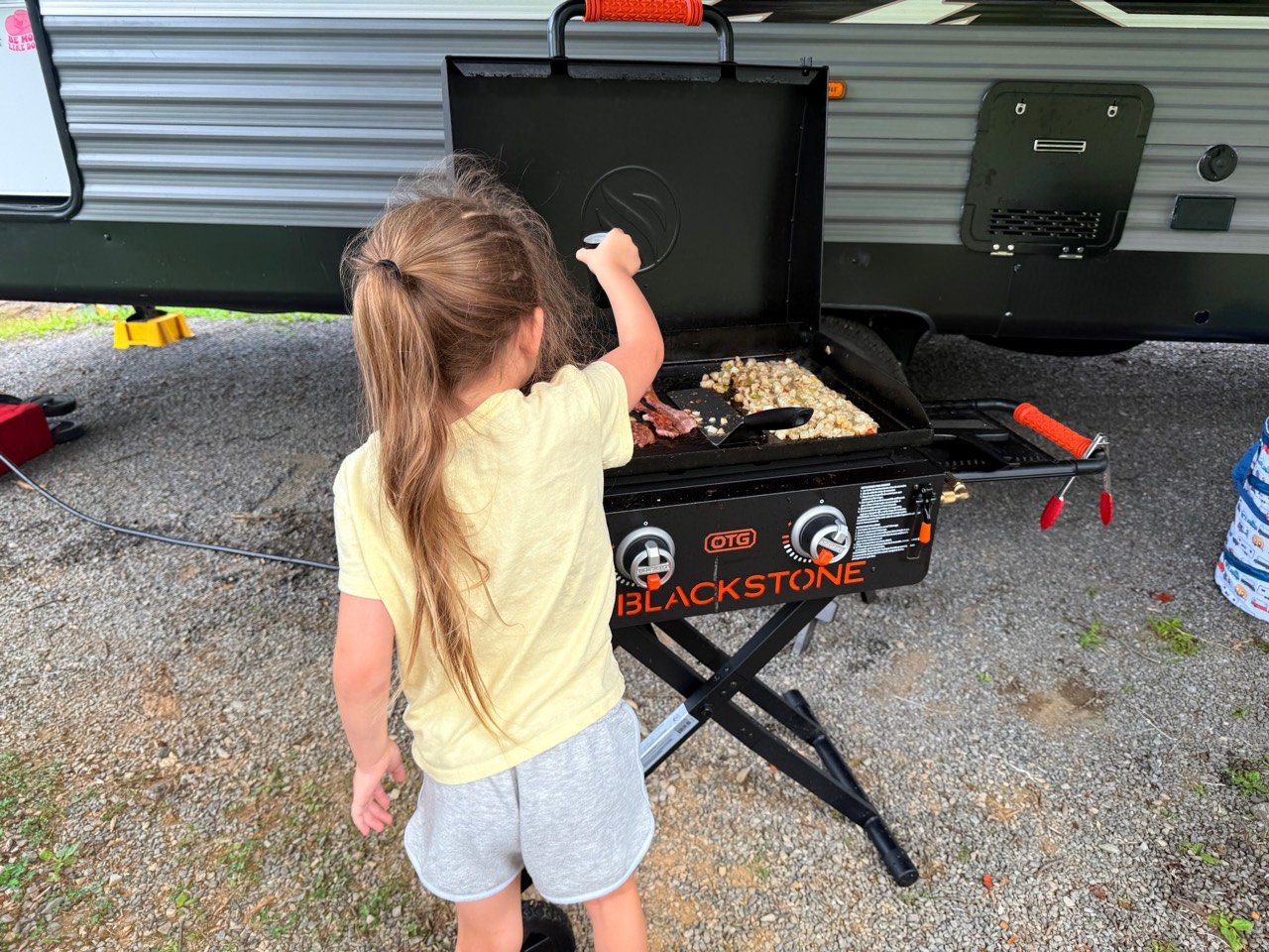 Our daughter helping cook bacon and breakfast potatoes on the Blackstone griddle at the campsite