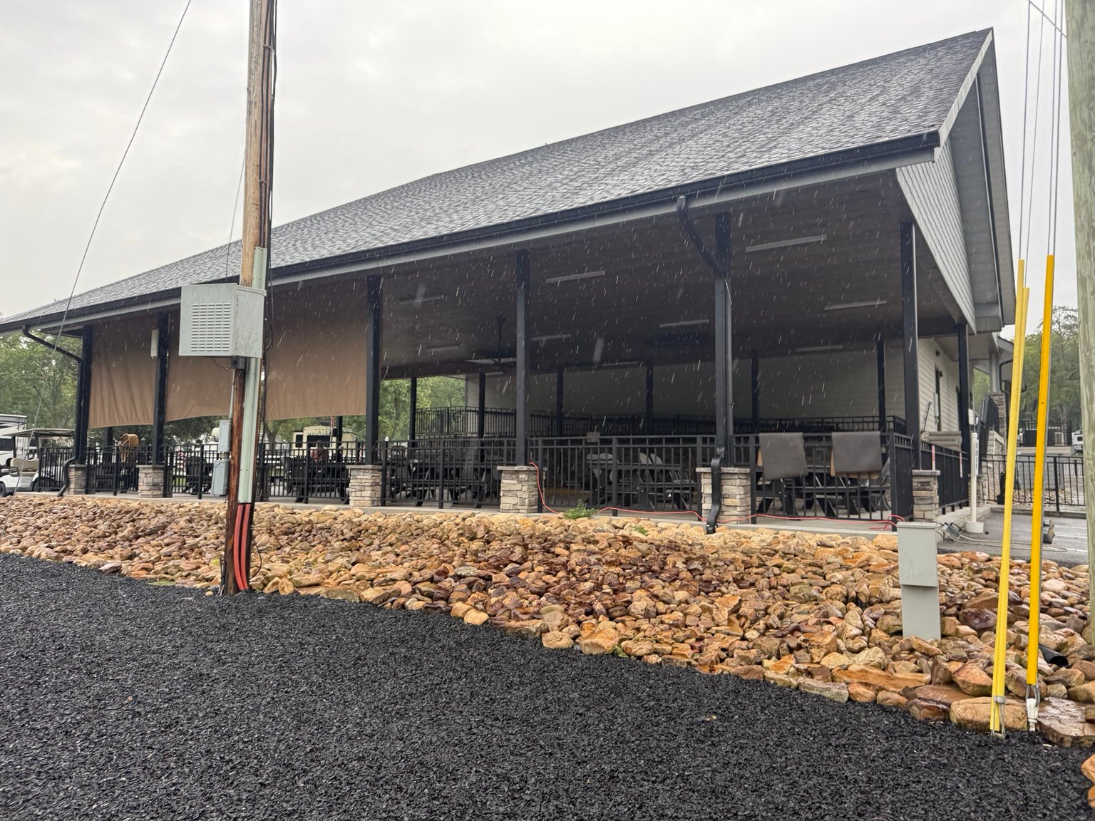 Large covered pavilion at Clabough's Campground with lowered weather screens, seating, and a landscaped stone border.